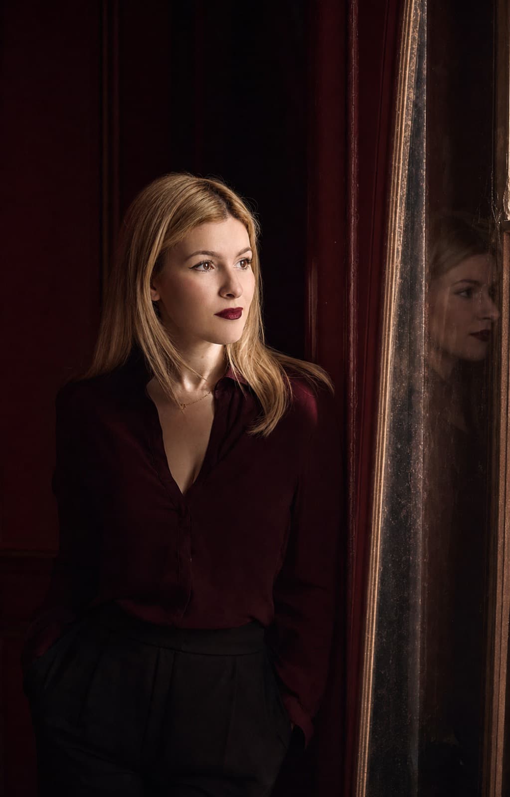 Kahina Belamri — founder of Chéri Social, photographed in profile against a bordeaux interior.